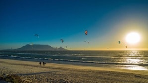 A beach with people walking and kites flying. - Sir David Baird 22 (Cape Town)