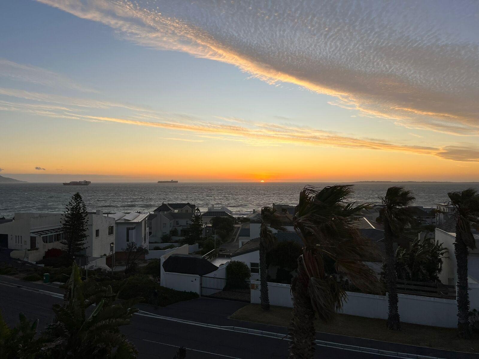 A coastal residential area with houses, a road, and a sunset over the sea.