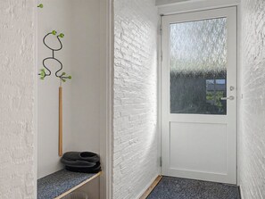 Een gang met een witte deur, een houten stok en een schoenenrek.