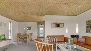 Een moderne woonkamer met houten plafond, een eethoek met tafel en stoelen, een bank en een salontafel.