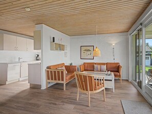 Un intérieur moderne avec un plafond en bois, un coin repas doté d’une table blanche et une cuisine avec des meubles blancs.
