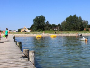Une jetée en bois s’étendant dans une eau calme, avec des pontons flottants jaunes, entourée d’arbres et de maisons.