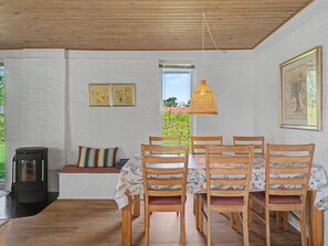 Un coin repas avec une table et des chaises en bois, un luminaire suspendu et une fenêtre donnant sur un paysage verdoyant.