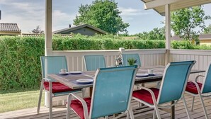 Een terras buiten met een tafel en stoelen, omringd door een houten terras en een overdekt gedeelte.