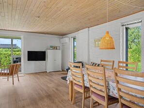 Een eetgedeelte met houten stoelen en een tafel, een televisie aan de muur en een hanglamp.