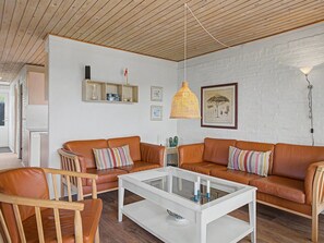 A modern living room with a white brick wall, two leather sofas, a glass coffee table, and a hanging wicker light fixture.