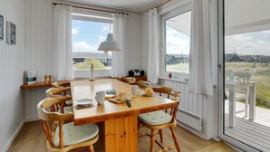 Un coin repas avec une table et des chaises en bois, un luminaire suspendu et de grandes fenêtres avec des rideaux.