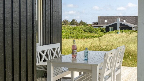 Une terrasse en bois avec une table et des chaises, donnant sur une pelouse et des bâtiments en arrière-plan.