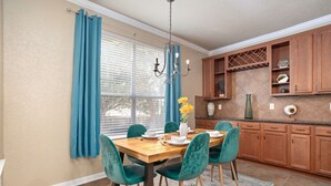 Un comedor con una mesa de madera, sillas azul verdosas y un jarrón con flores amarillas.
