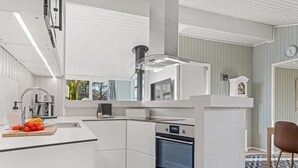 A modern kitchen with white cabinetry, a built-in oven, and a central island with a sink and a bottle of wine. - "Halwarth" - 250m from the sea by Interhome (Jerup)