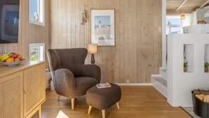 Una sala de estar con una pared de madera, un televisor, una silla, un pequeño taburete, un cuenco de fruta y un cuadro enmarcado.