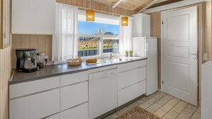 Una cocina con ventana, gabinetes blancos, un lavamanos y una cafetera.