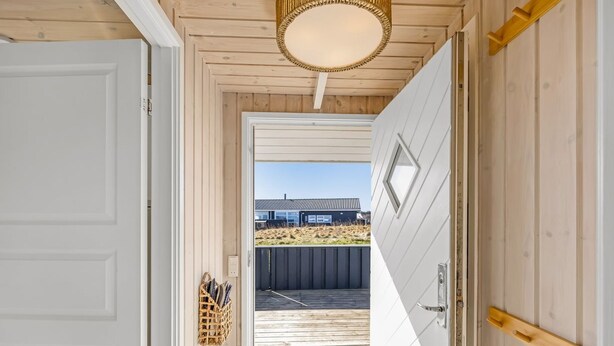 Un pasillo interior de madera con una puerta que da al exterior, una lámpara en el techo y un pequeño espacio exterior visible a través de la puerta.