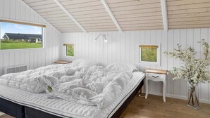 Une chambre à coucher comprenant un lit, une table de chevet, une commode, une fenêtre et une lampe fixée au mur.