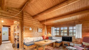 Ein gemütliches Blockhauss-Interieur mit Holzvertäfelung, einer Couch, einem Fernseher und einem Essbereich.