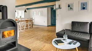 Un salon doté d’un poêle à bois, d’un canapé en cuir, d’un coin repas avec une table et des chaises, et d’œuvres d’art encadrées accrochées aux murs.