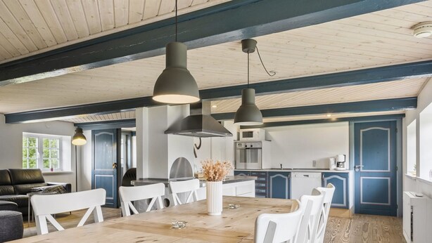 Une cuisine spacieuse avec une table en bois et des chaises blanches, un coin repas avec une grande fenêtre, et une cuisine moderne avec des meubles bleus et un four encastré.