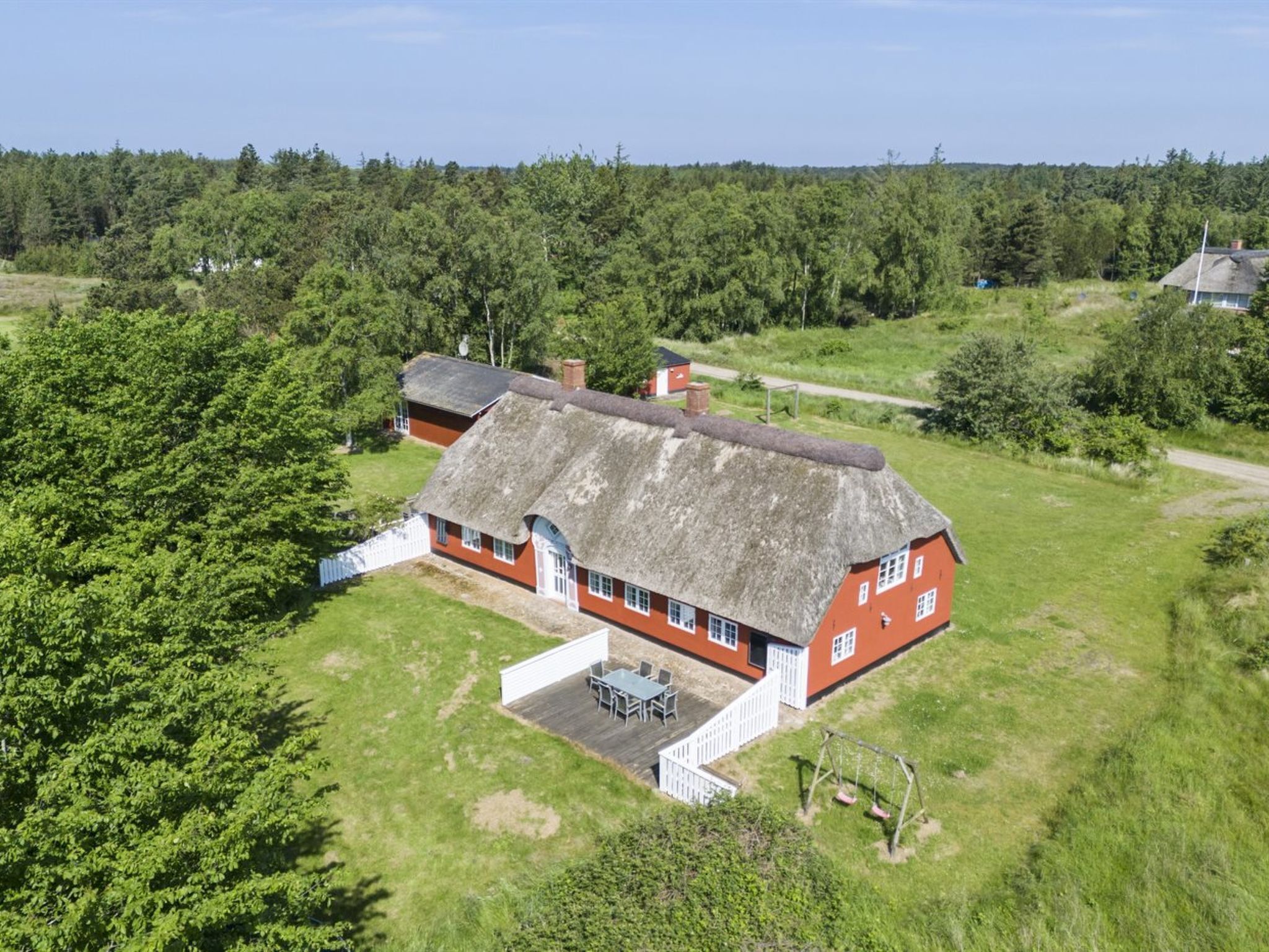 A red house with a thatched roof, surrounded by a grassy yard and trees.
