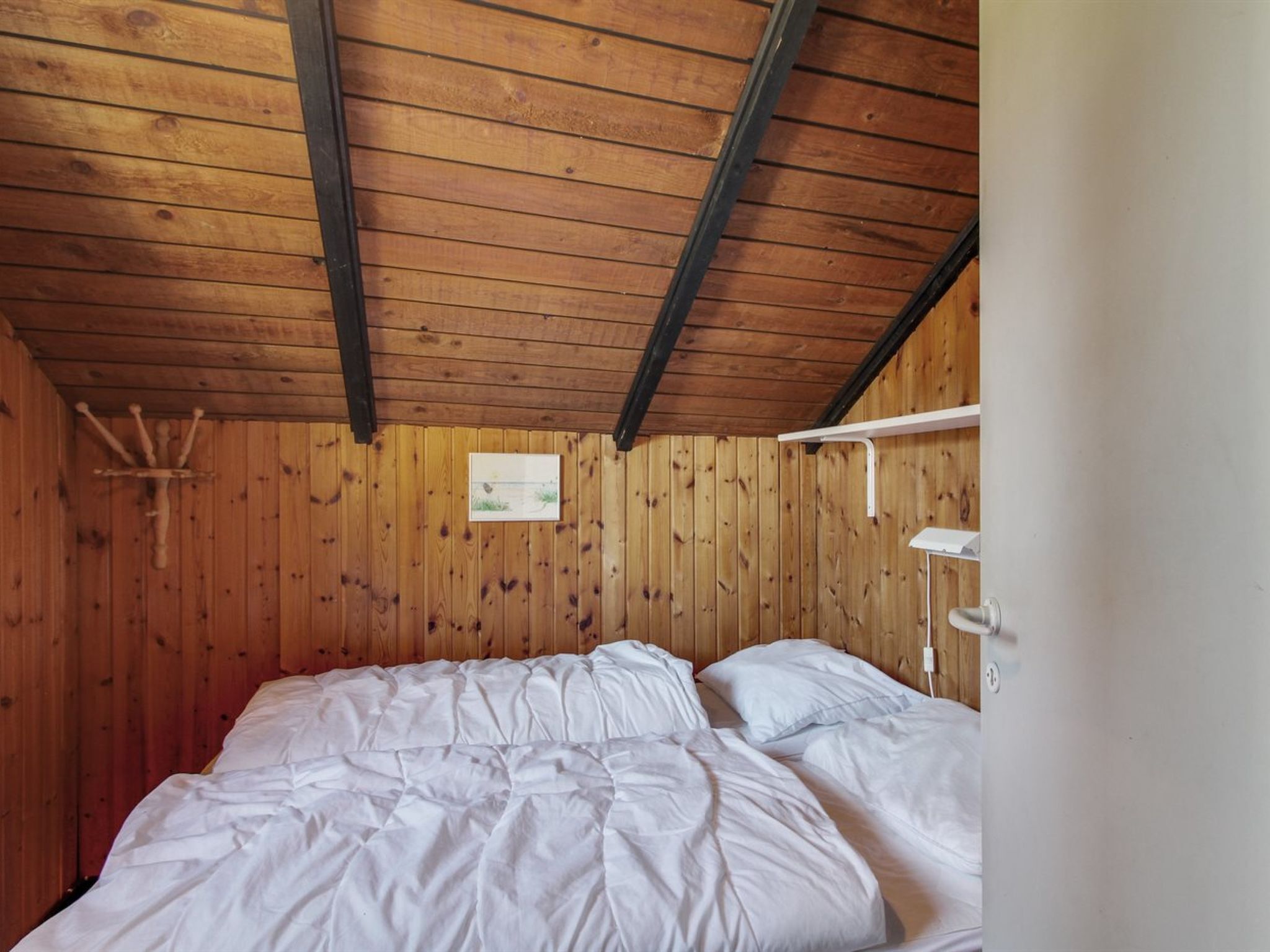Ein Zimmer mit Holzwänden, einem Bett, einem weißen Regal und einem an der Wand hängenden Bild.
