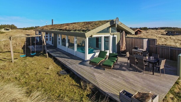 Ett trädäck med ett poolområde som är inbyggt i glas, utomhusmöbler och utsikt över det omgivande landskapet.