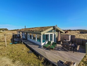 En træterrasse med et poolområde med glasafskærmning, udendørs møbler og udsigt over det omkringliggende landskab.