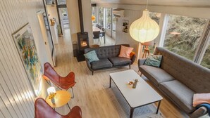 Ett modernt vardagsrum med en öppen spis, läderfåtöljer, en soffa och ett stort fönster med utsikt över omgivningen.