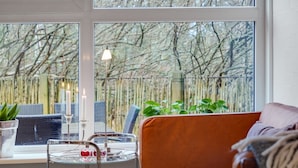 Ein gemütliches Wohnzimmer mit einer Couch, einem Glastisch mit Dekoration und Blick auf eine Bambusumzäunung durch große Fenster.