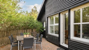 Eine Terrasse mit Tisch und Stühlen, ein Holzzaun und ein Haus mit großen Fenstern.