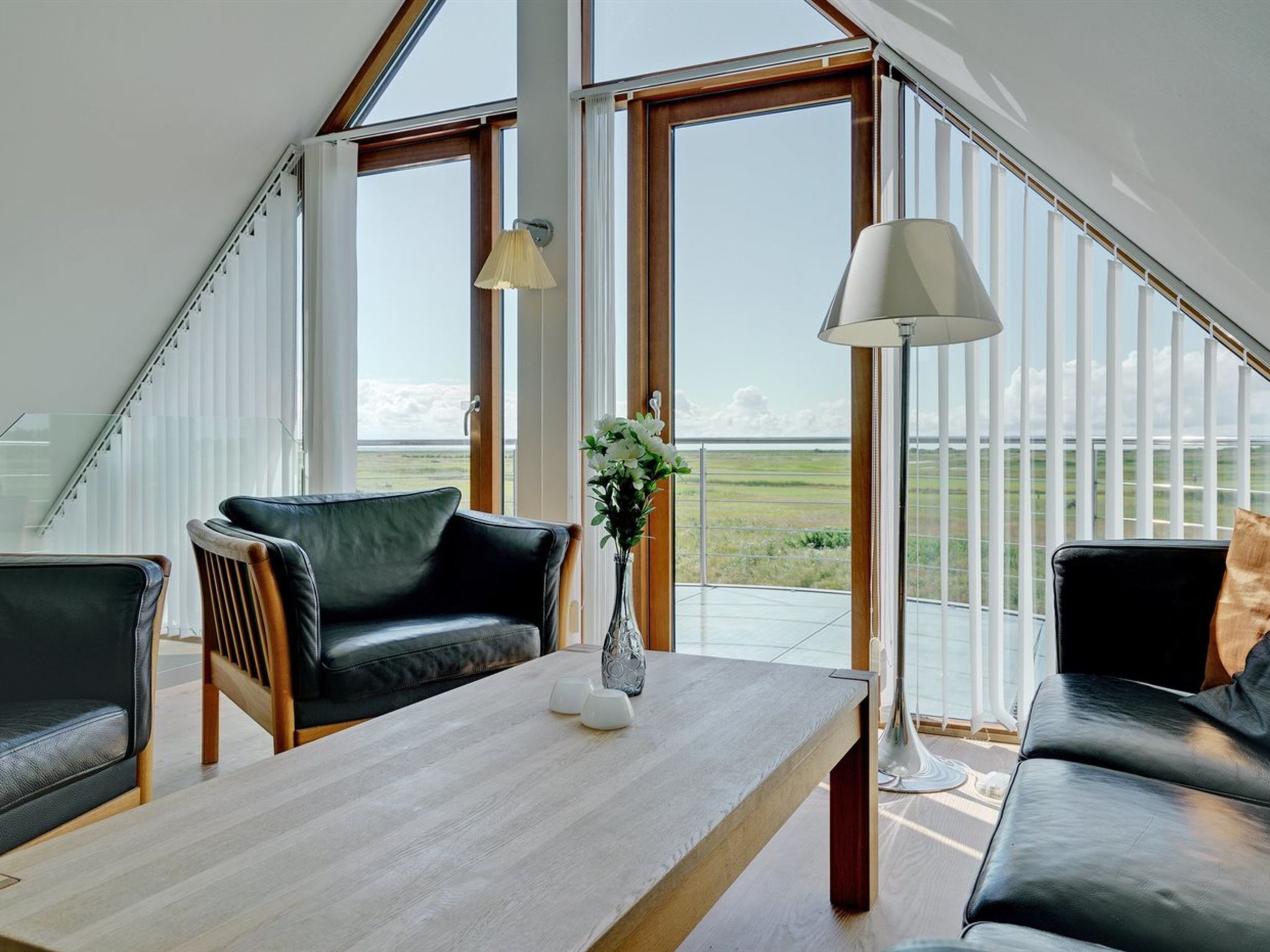 Un salon moderne avec une table en bois, des canapés en cuir noir et de grandes fenêtres donnant sur la campagne.