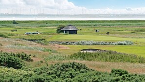 Golfkenttä, jossa on pieni rakennus, lampi ja taustalla näkyviä tuulivoimaloita.