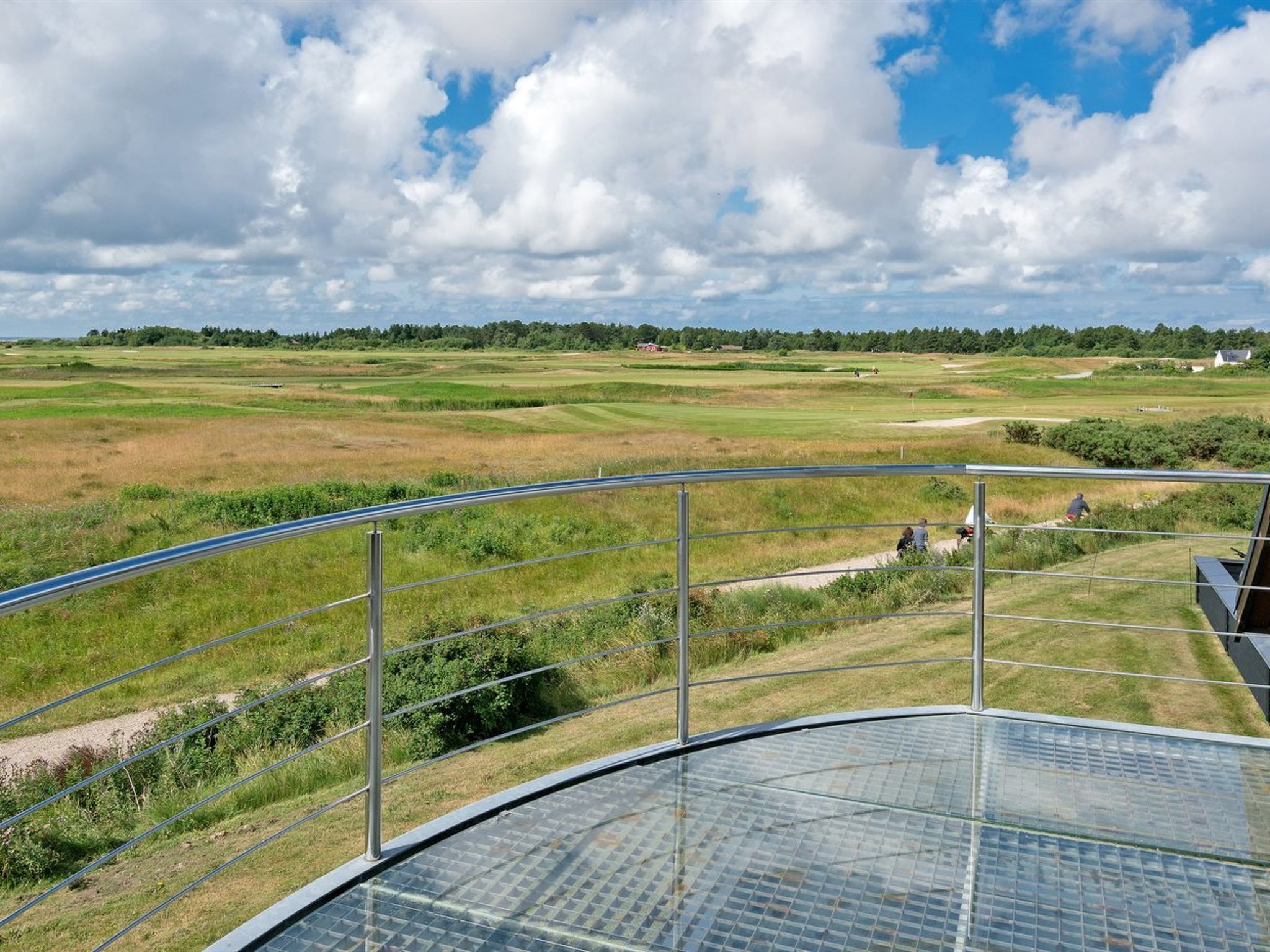 Fantastisk panoramaudsigt fra en balkon med gelænder, over en golfbane med grønne baner og en klar himmel.