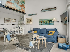 Un salon moderne avec un canapé bleu, des fauteuils en osier, une table à manger et des œuvres d’art accrochées aux murs.