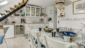 Una cucina moderna con mobili bianchi, un'area pranzo con sedie bianche, una scala e una lampada a sospensione.