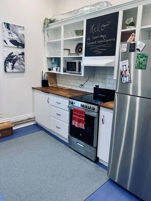 A modern kitchen with white cabinets, a stainless steel refrigerator, a built-in oven, and a chalkboard with a welcome message. - Pet-Friendly Space, King bed, Office (Halifax)