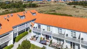 Un grand bâtiment blanc, doté d’un toit recouvert de tuiles rouges, de nombreux balcons et d’un vaste espace extérieur aménagé en terrasse.