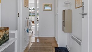 Un couloir doté d’un plancher en bois, de murs blancs, d’un porte-manteau suspendu, d’un tableau encadré, d’un radiateur et d’une porte donnant sur un espace extérieur.
