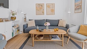 Un salon moderne avec un canapé gris, une table basse en bois et une bibliothèque. Deux reproductions botaniques encadrées ornent le mur.