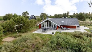 Een modern huis met een schuin dak, een terras met tuinmeubilair en een omliggend natuurlandschap.