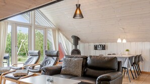 Een ruime woonkamer met een hoge plafond, leren banken, een eettafel en een open haard.