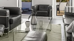 Ett modernt vardagsrum med lädersoffor, ett soffbord i glas och utsikt över naturen.