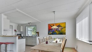 Een moderne keuken met een eethoek, met een houten tafel en stoelen, een kleurrijk abstract schilderij en uitzicht op het landschap.