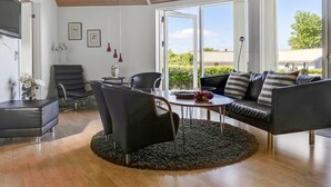 Un salon moderne avec un plafond en bois, un canapé en cuir noir, un fauteuil en cuir noir, une table basse ronde et un téléviseur placé sur le mur de gauche.
