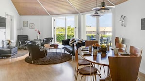 Un vaste espace de vie agrémenté d’un plafond en bois, d’une table à manger pour quatre personnes et d’un coin salon confortable.
