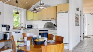 Une cuisine moderne avec des meubles en bois, un four encastré et un coin repas comprenant une table ronde et des chaises.