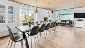 A spacious living area with a wooden ceiling, a dining table with chairs, a sofa, and a TV.