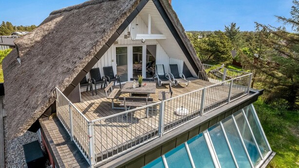A modern house with a thatched roof, a deck with outdoor seating, and a swimming pool.
