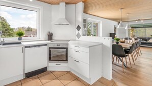 A modern kitchen with white cabinetry, a built-in oven, and a dining area with a wooden table and chairs.