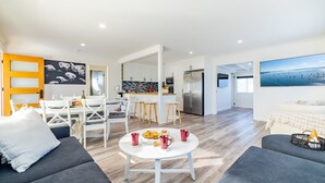 A modern living room with a dining area, kitchen, and a large window with a view of the sea. - The Pacific Pearl,16 Pacific Avenue, Anna Bay - pet friendly, air con (Anna Bay)