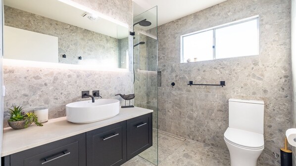 A modern bathroom with a large mirror, a white sink, dark cabinets, a toilet, and a shower area.