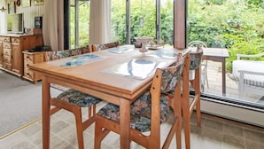 Un espace repas avec une table et des chaises en bois, un luminaire suspendu et une vue sur la verdure à l’extérieur.